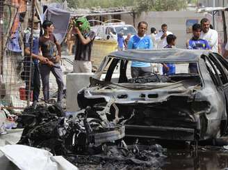 <p>Pessoas se reúnem em volta de um carro-bomba, perto de Basra. O carro explodiu perto da cidade xiita, nesta quarta-feira</p>
