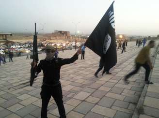 <p>Um integrante do Estado Islâmico exibe uma bandeira do grupo terrorista em uma rua da cidade de Mossul, em 23 de junho</p>