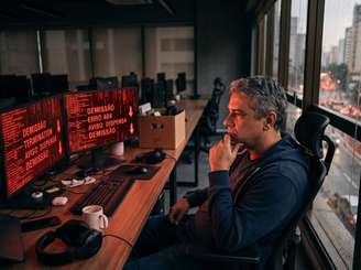 Homem pensativo em escritório vazio de game studio. Monitores simbolizam demissões no setor e incertezas sobre jogos AAA.