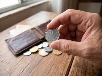 Imagem mostra uma mão mostrando uma moeda de 50 centavos brasileira.
