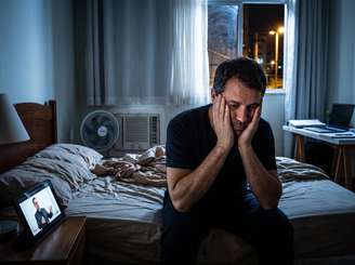 Imagem mostra homem com insônia em seu quarto durante a madrugada.
