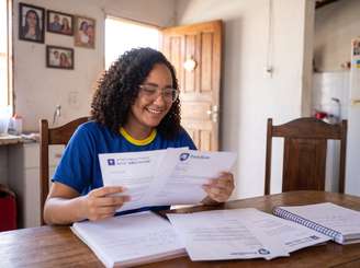 Imagem mostra aluna brasileira com cartas de aprovação de universidades internacionais na mão.