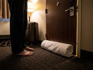 Imagem mostra toalha enrolada tampando a fresta da porta de um quarto de hotel.