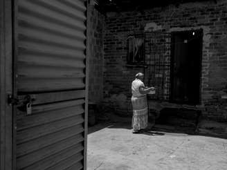 <p>Mulher carrega panela com água para sua cada na favela de Alexandra, em Johannesburgo, na África do Sul. Água e o banheiro - porta do lado esquerdo - é dividido por cerca de 250 moradias.</p>