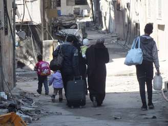 Civis levam seus pertences enquanto caminham até um ponto de encontro para serem evacuados da zona citiada de Homs