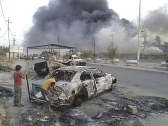 <p>Crianças observam carro queimado durante confrontos em Mossul, no norte do Iraque, em 2014</p>