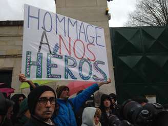 Homem carrega cartaz "homenagem a nossos heróis" em frente ao cemitério de Montparnasse