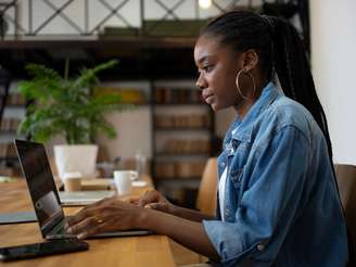 A imagem mostra uma mulher negra, entre o público alvo do curso de marketing, usando um notebook em local de trabalho