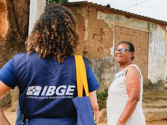 A imagem mostra uma censora do IBGE, negra, entrevistando uma senhora também negra