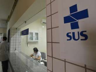 A imagem mostra a recepção de um hospital, com uma placa do Sistema Único de Saúde destacado