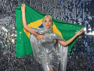 Imagem mostra Beyoncé com um vestido prateado e segurando a bandeira do Brasil.