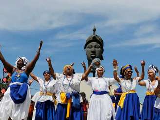 Na imagem, mulheres negras com vestimentas azul e branca, em frente a monumento de Zumbi dos Palmares