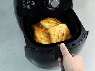 Na imagem há uma pessoa colocando fatias de pão congelado em uma air fryer para descongelar.
