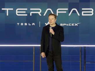 Elon Musk no centro, à frente de um telão com as logos da Tesla e SpaceX
