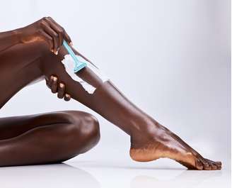 Mulher depilando a perna com a clássica lâmina; há alternativas de laser para pele retinta
