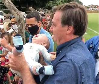 Jair Bolsonaro pega bebê nos braços durante viagem a Goianópolis; presidente voltou a dispensar o uso da máscara em compromisso público.