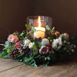 1. Arranjo de natal feito com folhagens, flores, pinhas e uma única vela no meio – Foto: Alaric Flowers