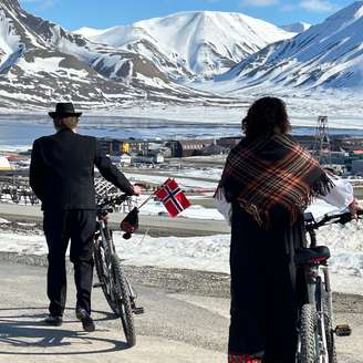 Noruegueses andando de bicicleta em Svalbard, com picos cobertos de neve ao fundo