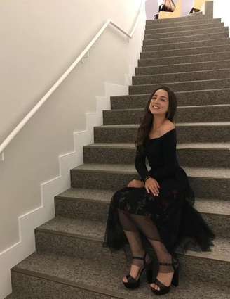 Samira com cabelo preto e vestido preto nas escadas.