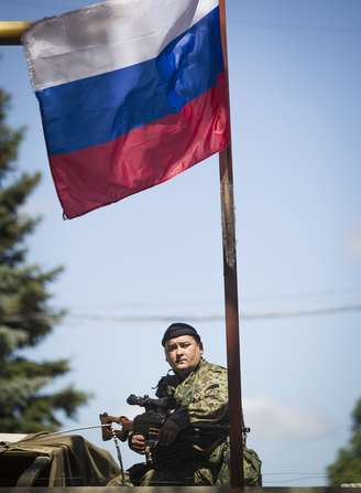 <p>Um separatista pró-russa armado senta debaixo de uma bandeira russa</p>