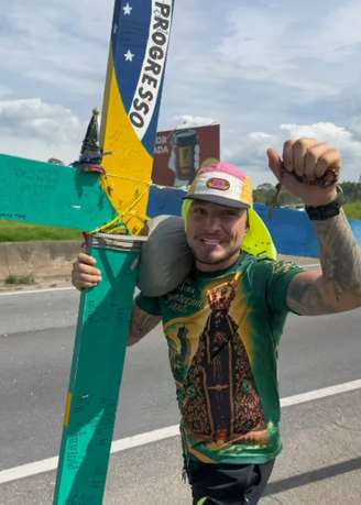 MC Gui ajuda o romeiro Júlio Mesquita a carregar cruz durante sua peregrinação à cidade de Aparecida.
