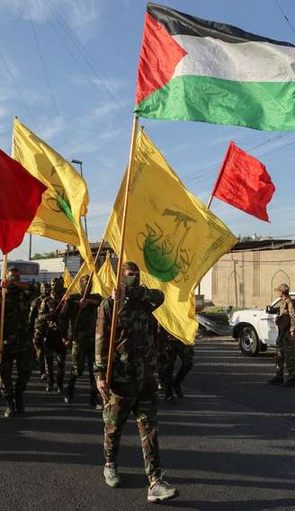 Membros do Harakat Hezbollah al Nujaba seguram uma bandeira palestina e outras bandeiras durante um protesto em solidariedade aos palestinos em Gaza